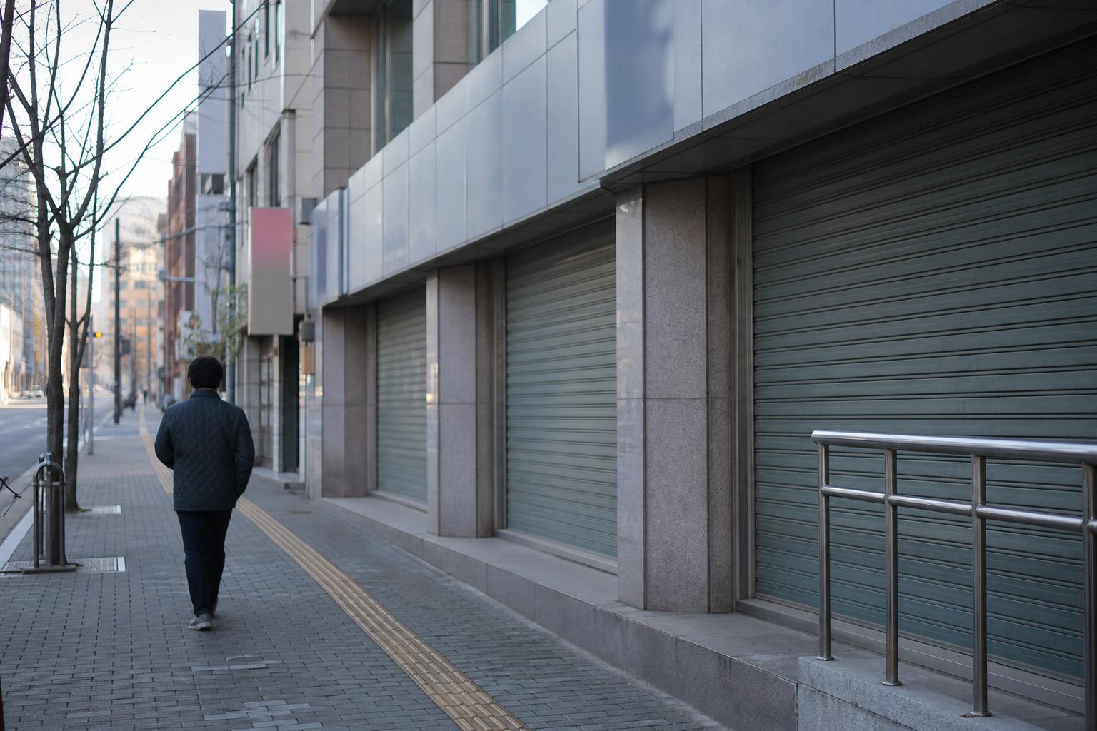 한산한 연휴 아침 은행 지점 앞 거리를 걷는 사람의 뒷모습