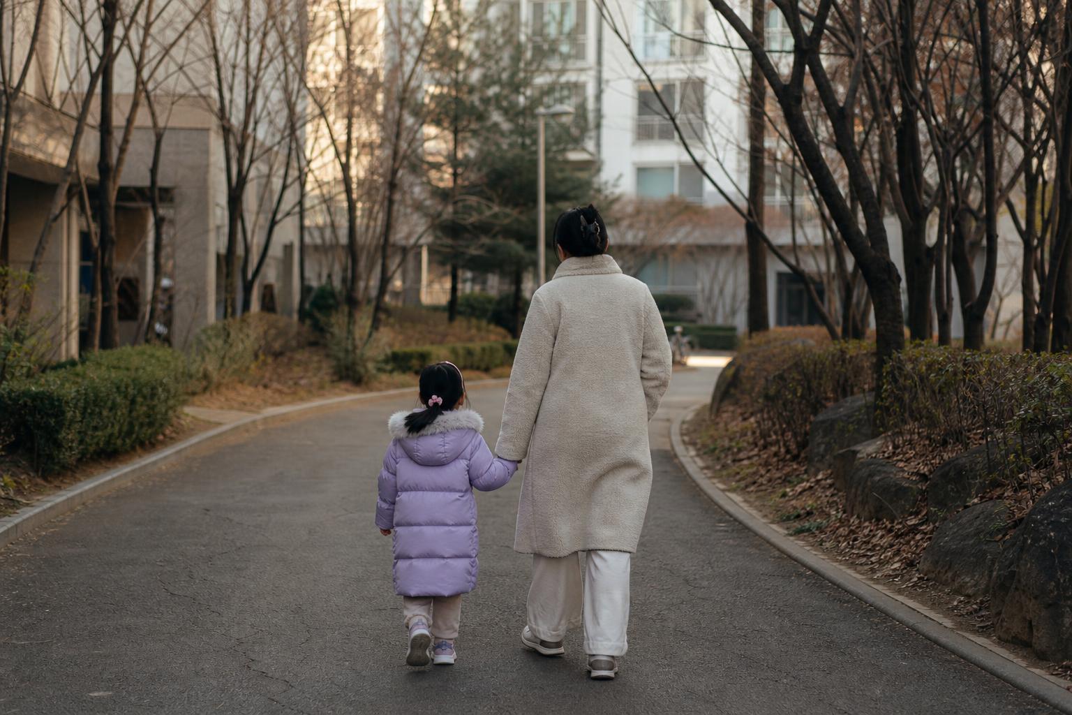 한국 아파트 단지 산책로를 아이와 함께 걸어가는 보호자의 뒷모습