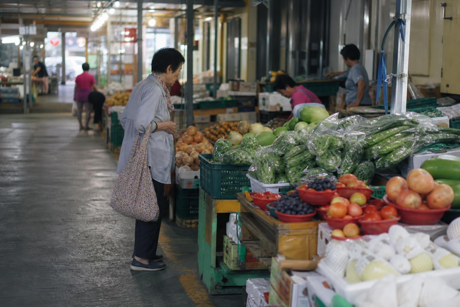이른 아침 동네 시장에서 채소 진열대 앞을 지나가는 사람의 옆모습