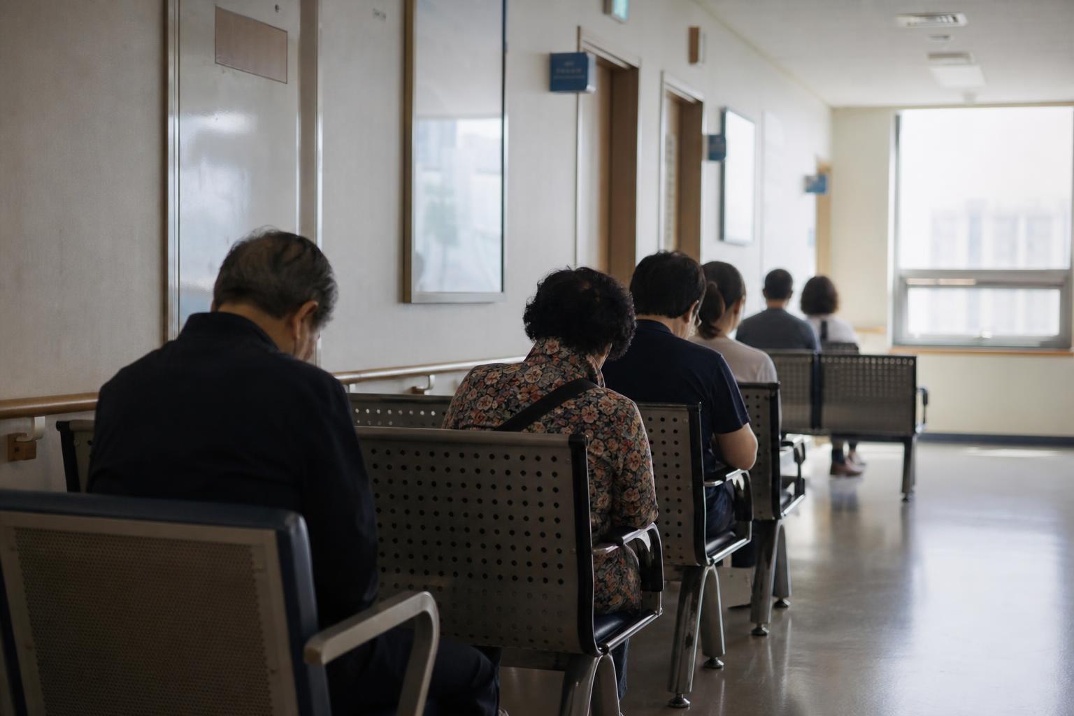 병원 접수 창구 앞 복도에 앉아 순서를 기다리는 사람들의 뒷모습