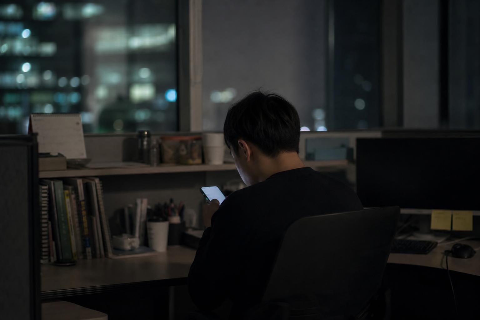 휴대전화를 들여다보는 사람의 뒷모습이 보이는 야간 사무실