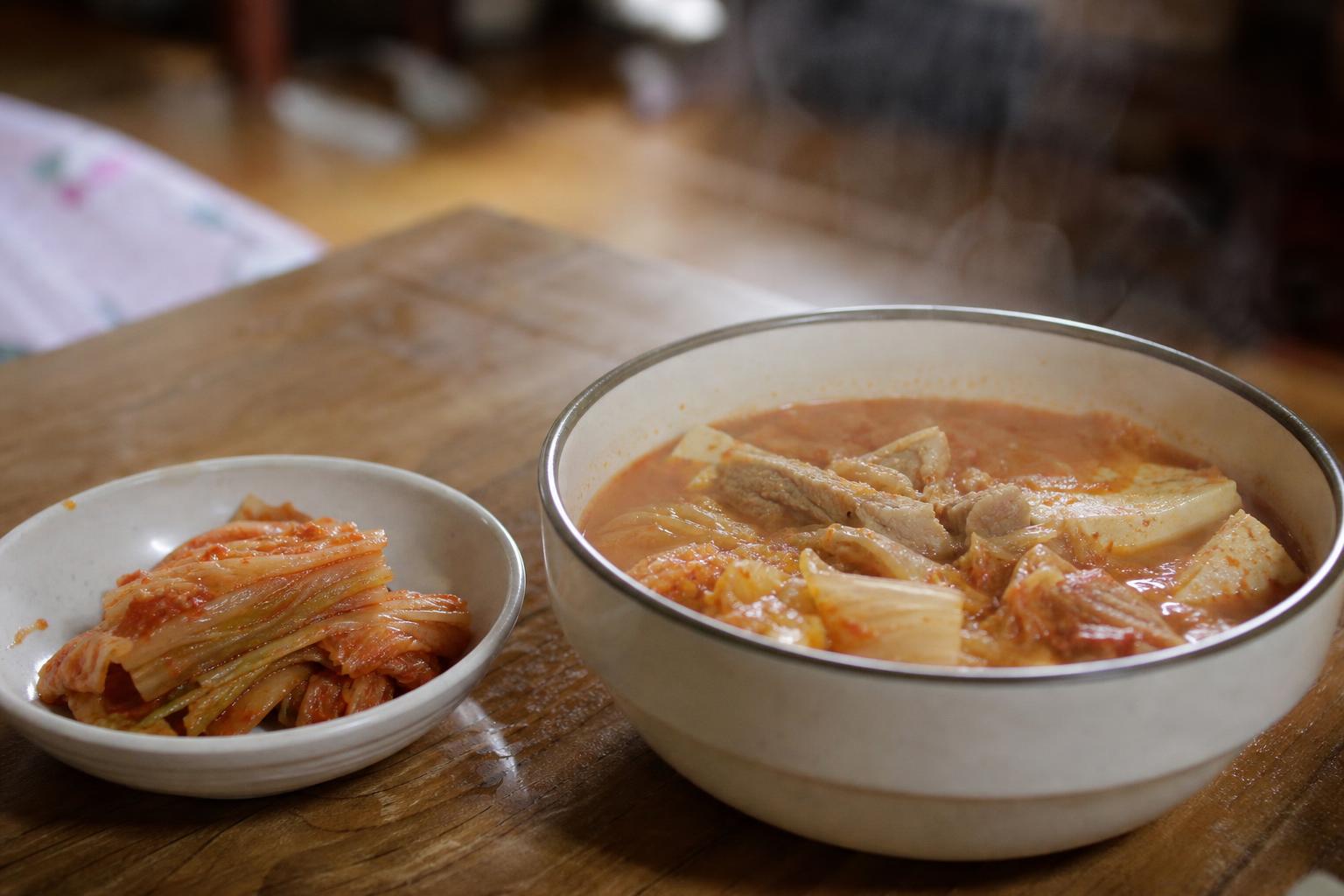 배추김치가 담긴 반찬 용기와 숟가락이 놓인 식탁