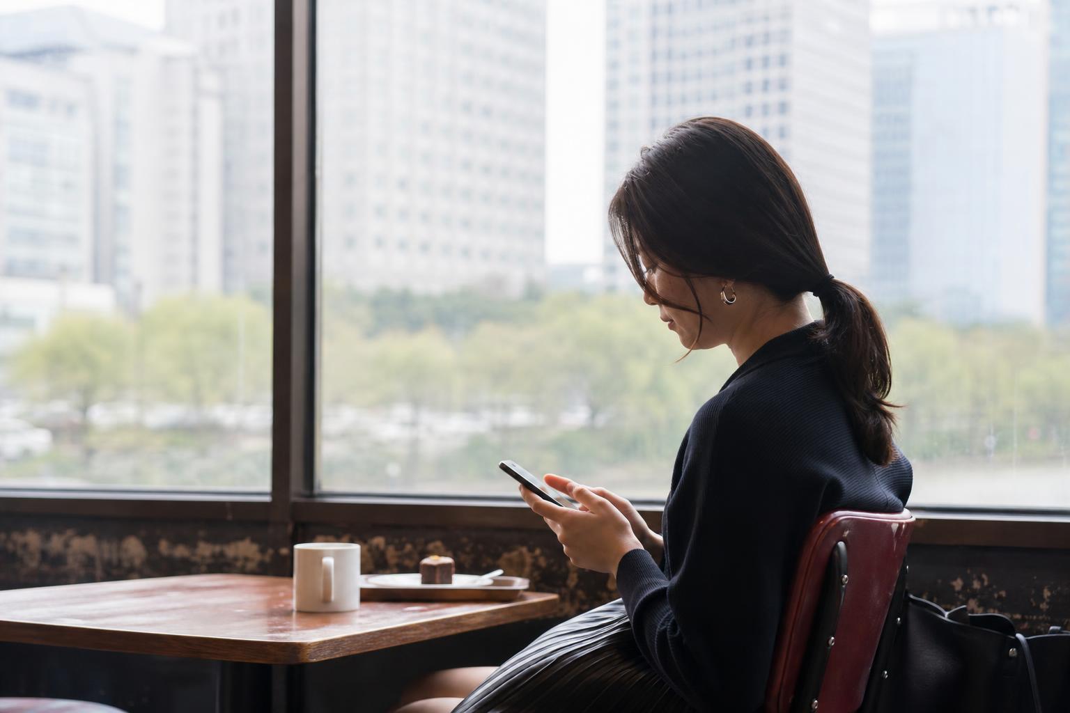 카페 창가에서 휴대전화를 들여다보는 사람의 옆모습