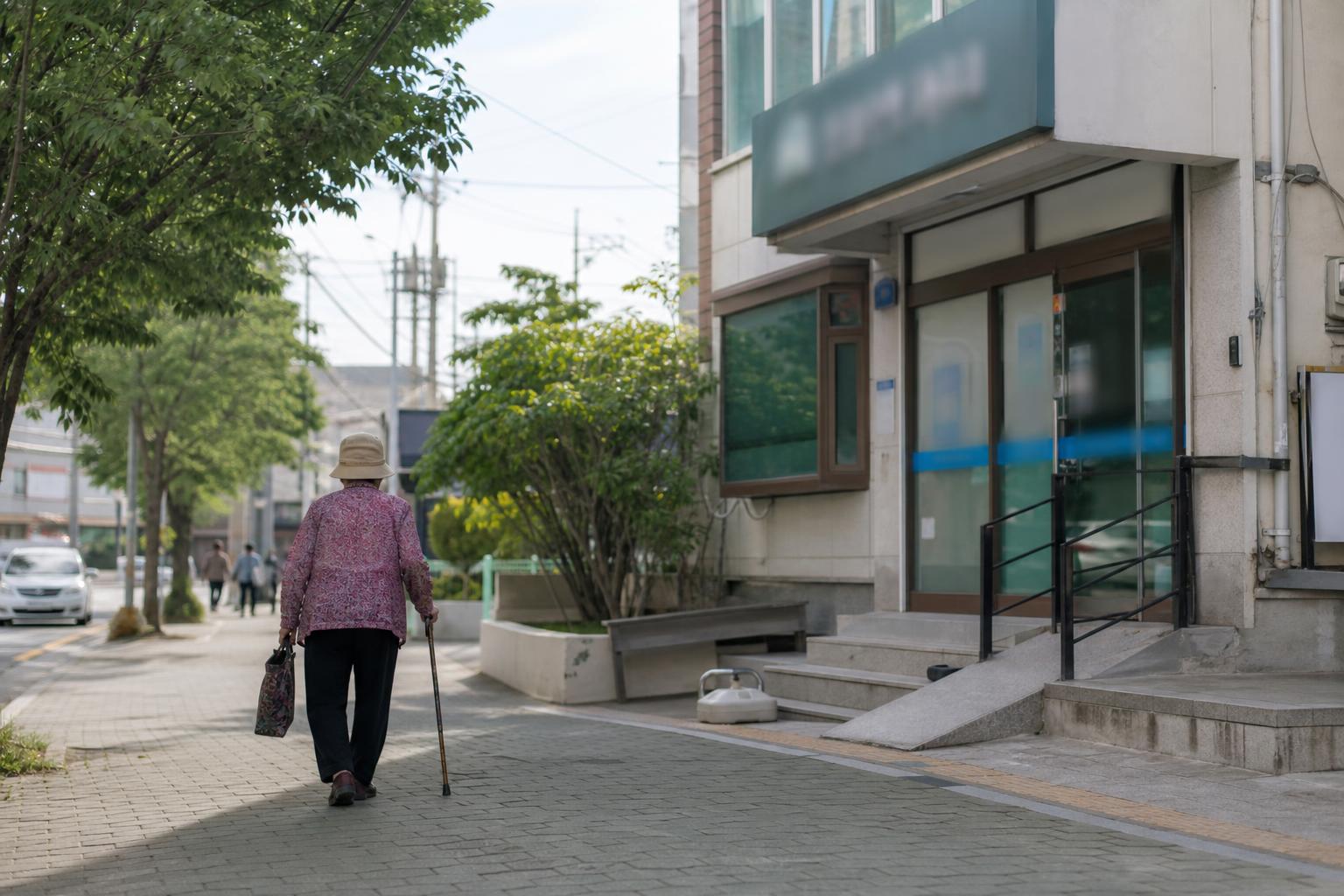 이른 오전 한국 동네 골목의 의원 건물과 걸어가는 어르신의 뒷모습