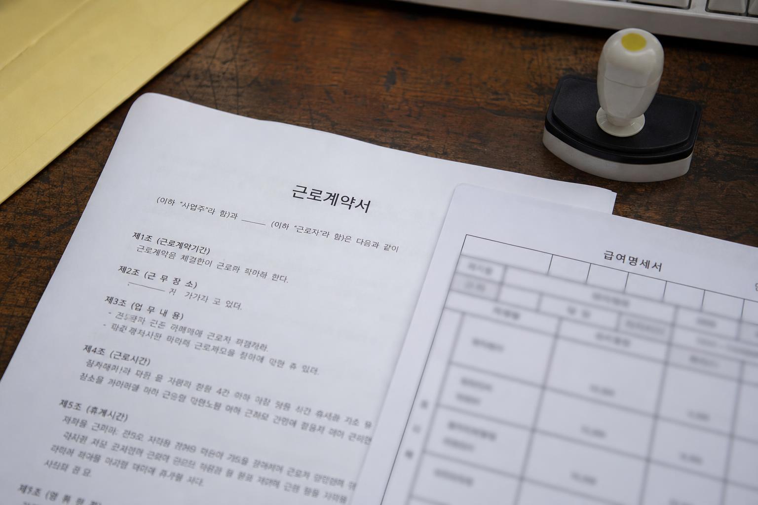책상 위에 놓인 근로계약서와 급여명세서, 도장
